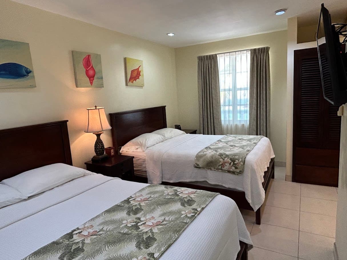 A well-appointed hotel room with two queen beds, each featuring a floral throw, a bedside table with a lamp, and colorful fish artwork on the wall.