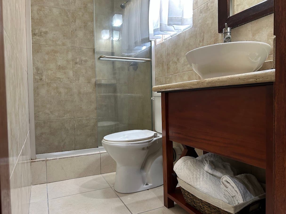 A clean, well-lit bathroom with a modern vessel sink on a wooden vanity, a toilet, and a glass-enclosed shower.
