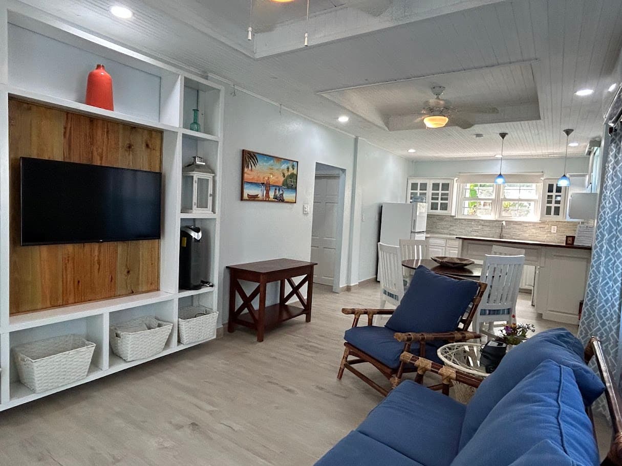 A modern open-plan living area with a large wall-mounted TV, comfortable seating, and a view of the adjacent, well-equipped kitchen.