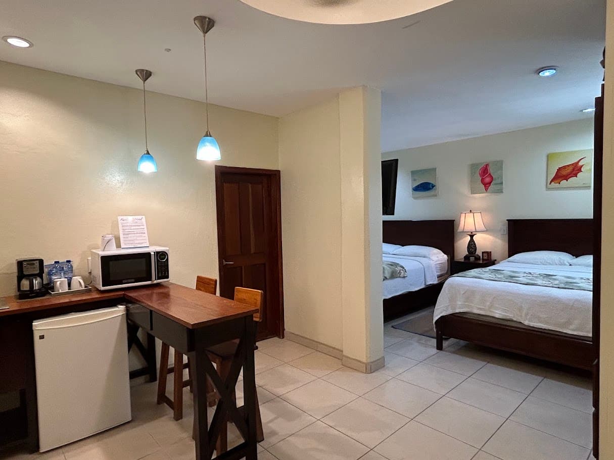 A hotel suite featuring a kitchenette with a microwave and mini-fridge, a breakfast bar, and a separate bedroom area with two queen beds.