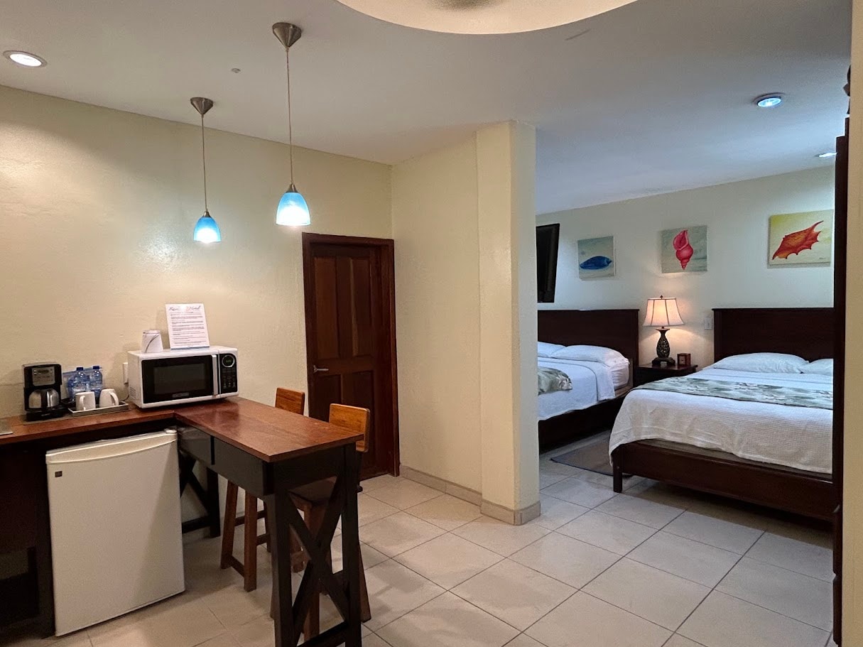 A hotel suite featuring a kitchenette with a microwave and mini-fridge, a breakfast bar, and a separate bedroom area with two queen beds.