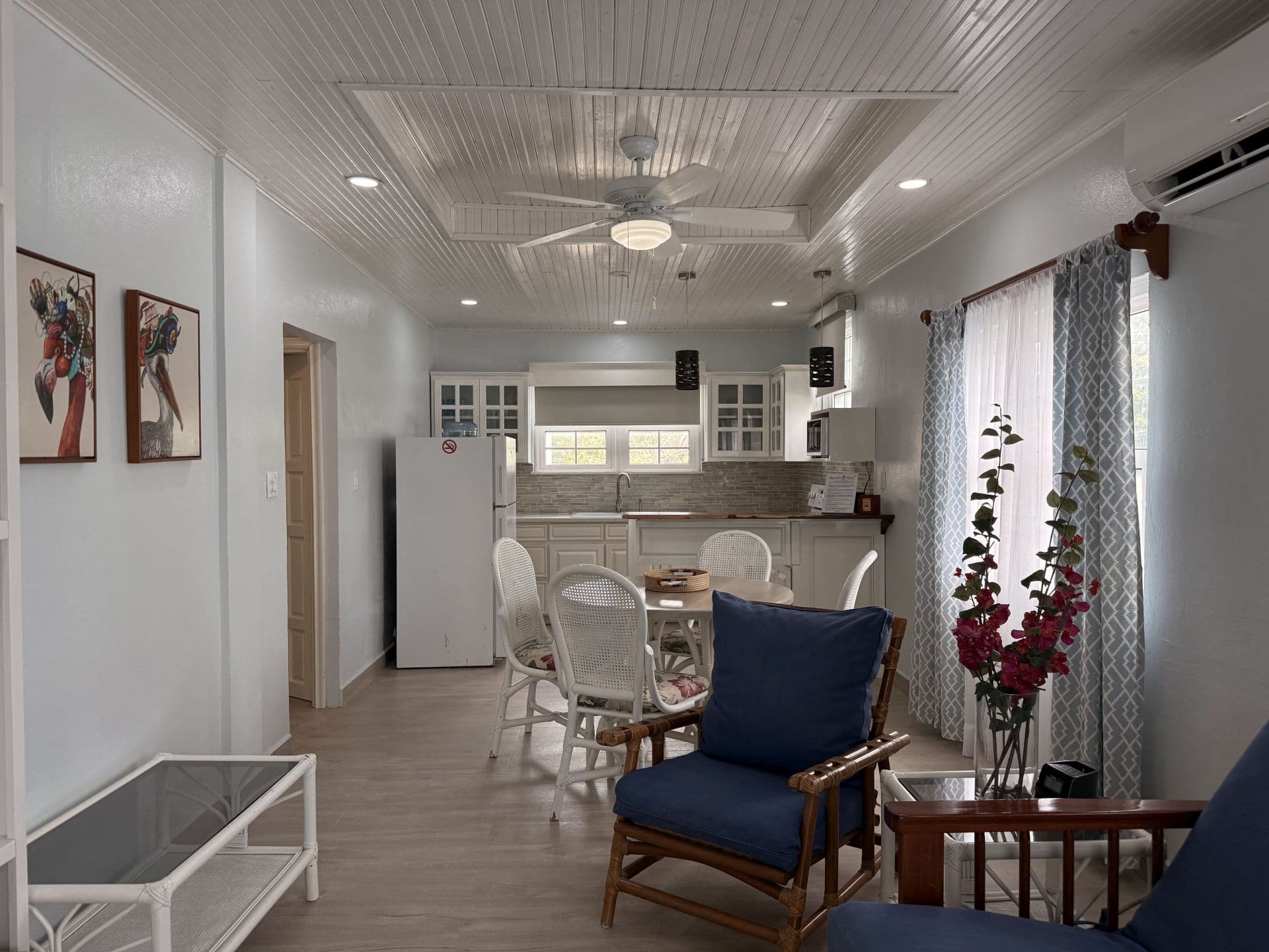 A spacious, light-filled open-concept living area with comfortable seating, a dining table, and a modern kitchen, all under a decorative ceiling.