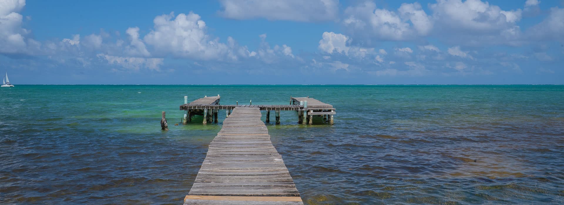 A wooden pier extends over calm, turquoise water under a partly cloudy sky.