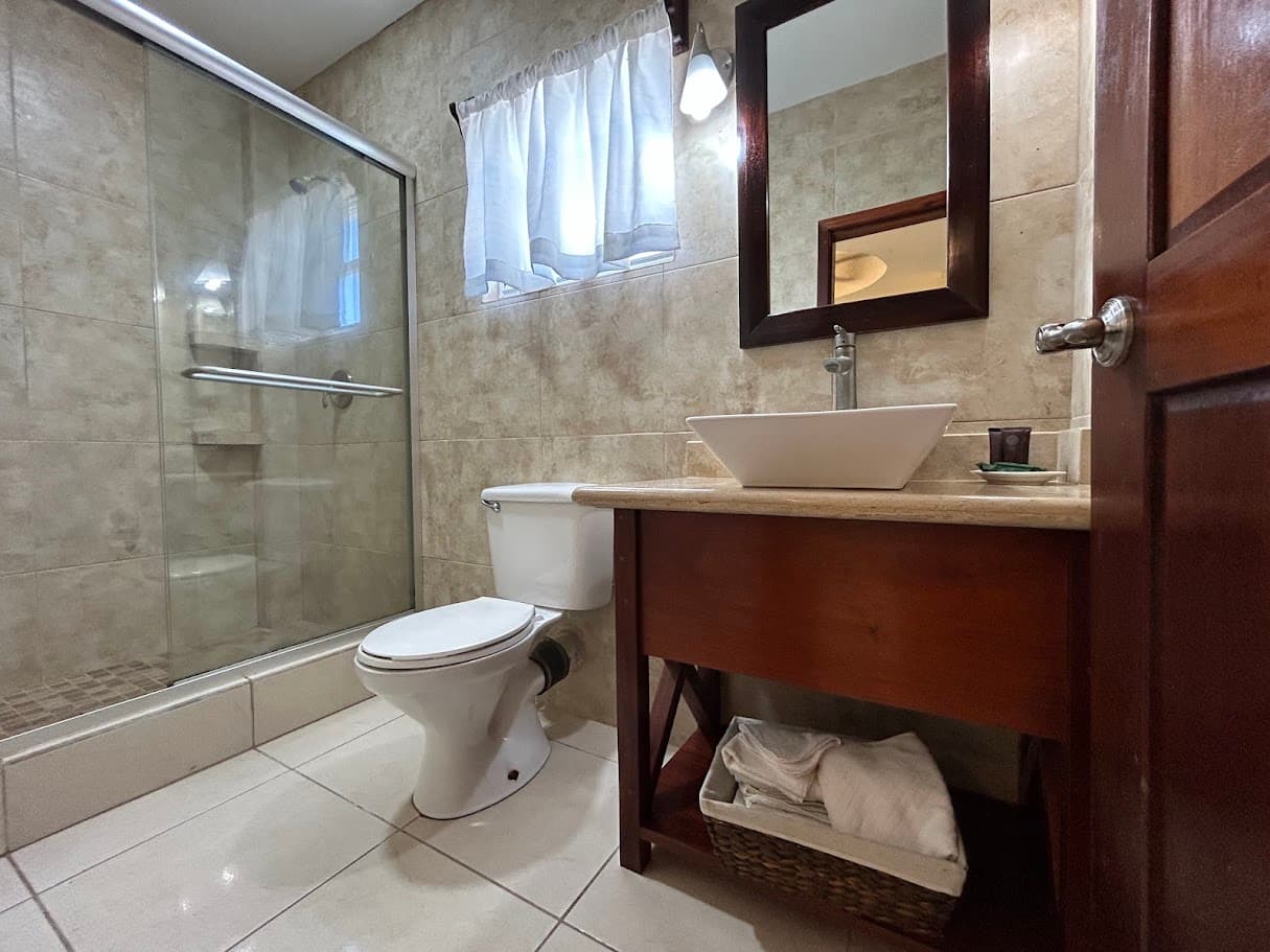 A well-appointed bathroom featuring a modern vessel sink on a wooden vanity, a toilet, a glass-enclosed shower, and tiled walls.